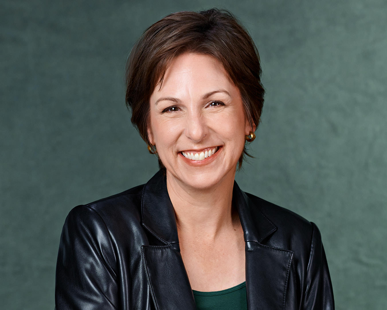 Professional woman in a leather blazer, smiling warmly against a green background.