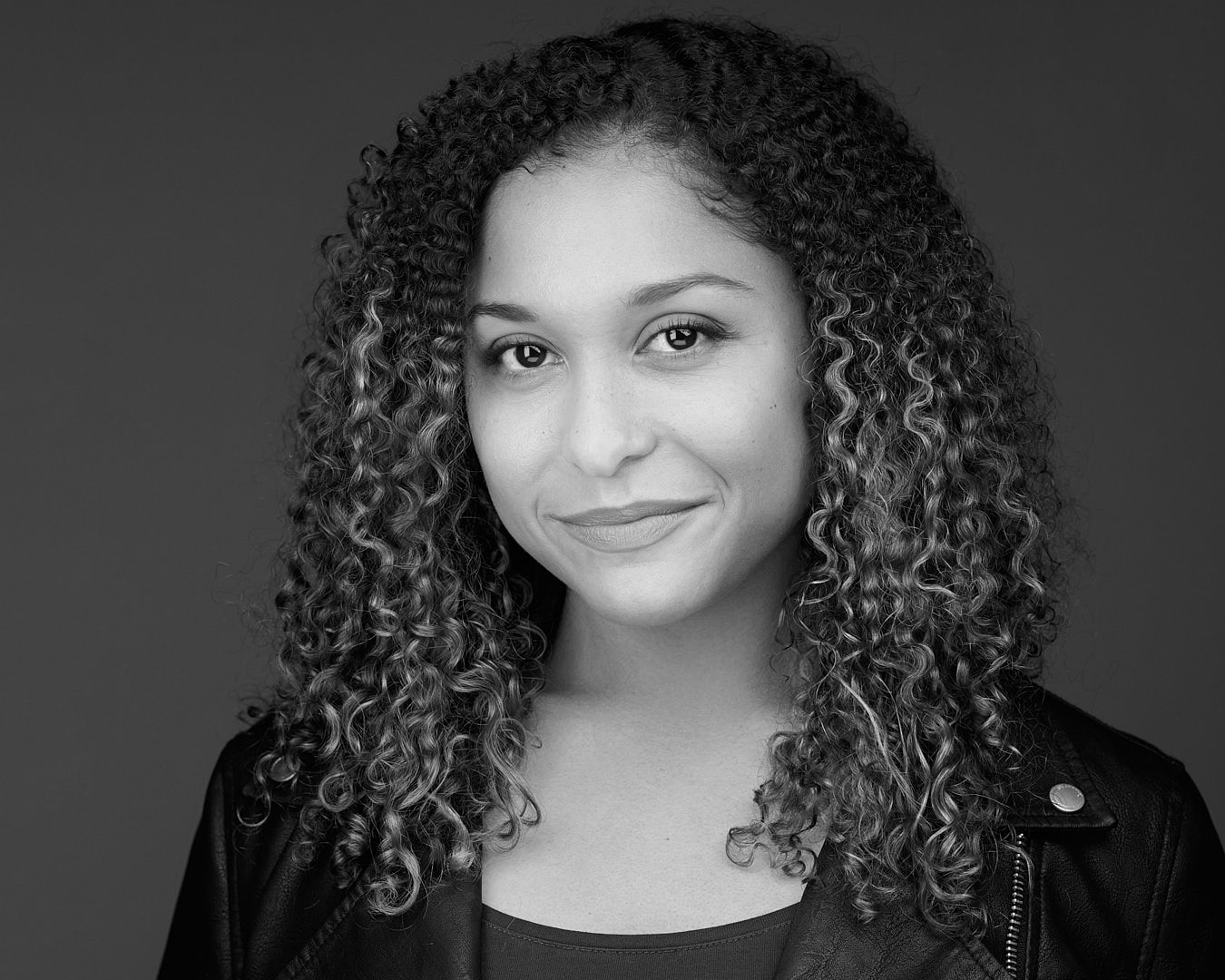 A black and white headshot of a young woman with curly hair, smiling confidently.