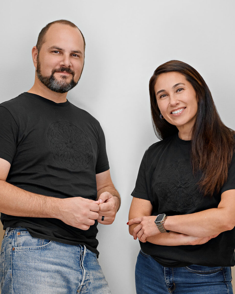 Two professionals smiling and standing side-by-side against a light, neutral background at Dean Birinyi Photography's Palo Alto studio, showcasing a casual yet polished look for new hire headshots.