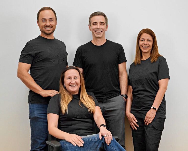 A team photo featuring startup executives and team leaders in Silicon Valley casually dressed in matching black shirts, smiling confidently against a neutral background.