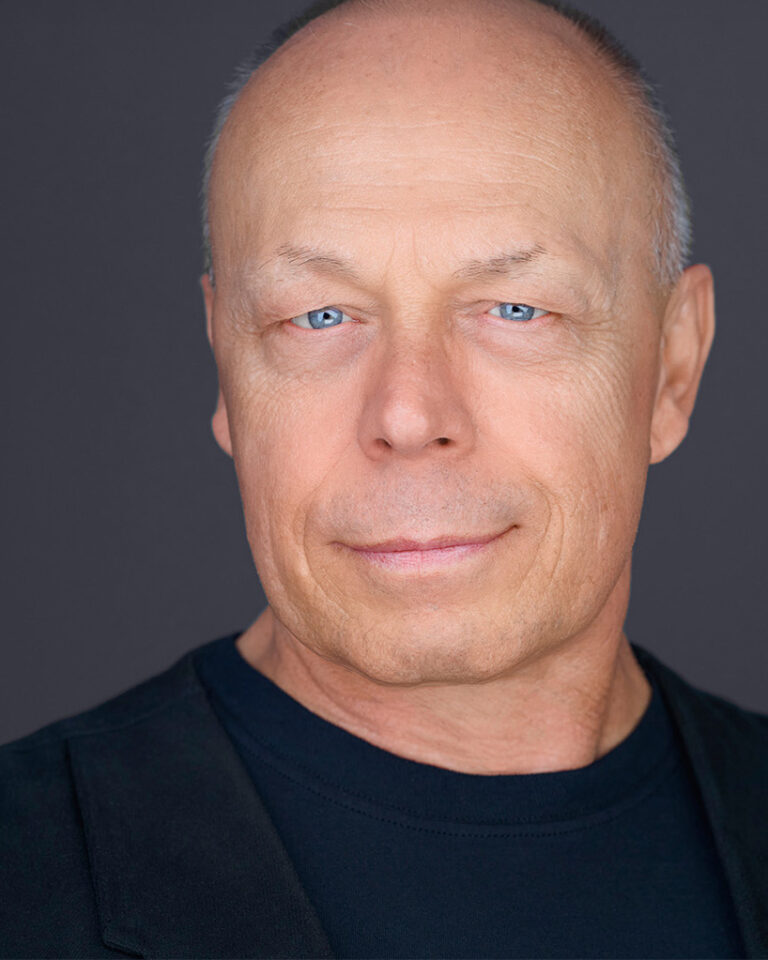 Professional headshot of Dean Birinyi with a confident and approachable expression, set against a clean, dark gray background.