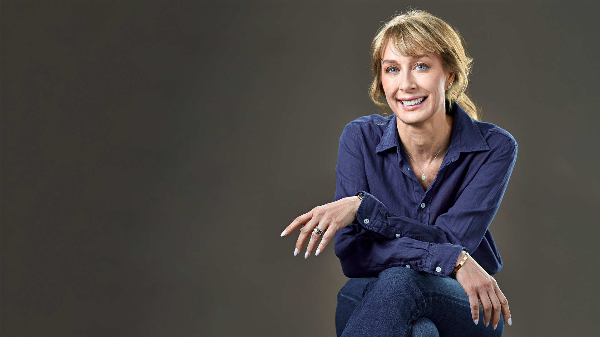 Professional headshot of a woman in a navy blue blouse and jeans, smiling confidently against a moody dark background, captured by Dean Birinyi in Silicon Valley