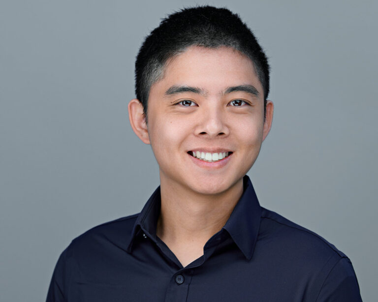 Professional headshot of a young man in a dark navy shirt, smiling confidently. Photographed by Dean Birinyi in Silicon Valley.