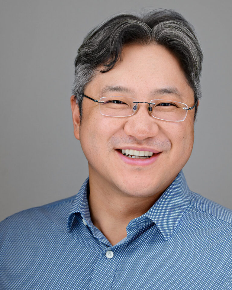 Smiling man in a blue patterned shirt and glasses, professionally photographed by Dean Birinyi for company headshots in Palo Alto.