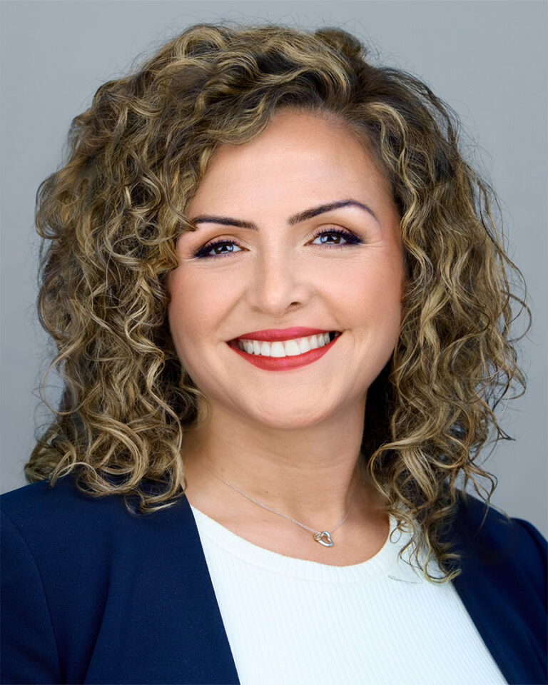 Smiling woman with curly hair in a navy blazer and white top, photographed by Dean Birinyi for a company headshot in Palo Alto.