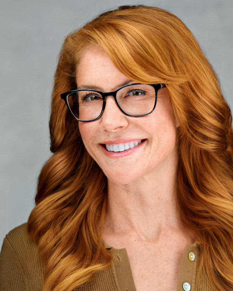 Professional headshot of a smiling woman with red hair and glasses, photographed by Dean Birinyi in Palo Alto.