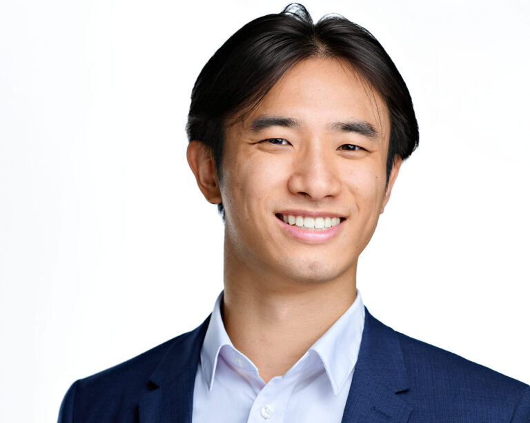 Professional headshot of a young man in a navy blazer and white shirt, smiling confidently. Photographed by Dean Birinyi in Palo Alto.