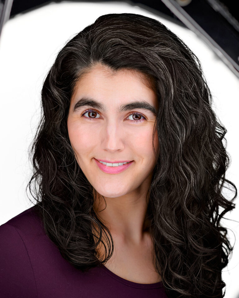 Professional woman with long curly hair smiling in front of a studio light setup.