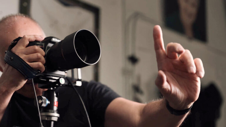 Photographer adjusting camera while directing a headshot session, hand raised mid-gesture, shot in-studio with shallow depth of field.