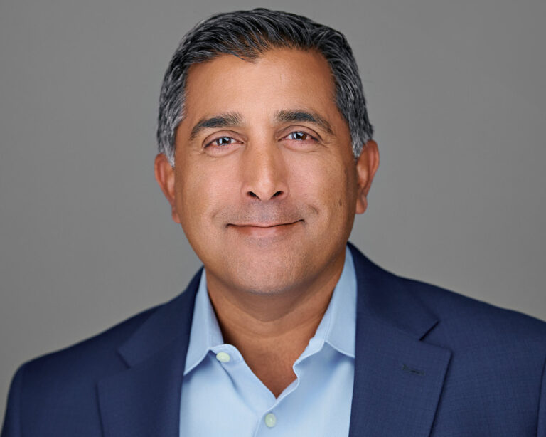 Professional man in a blue blazer and light blue shirt, looking composed and confident in a studio headshot with a gray background.