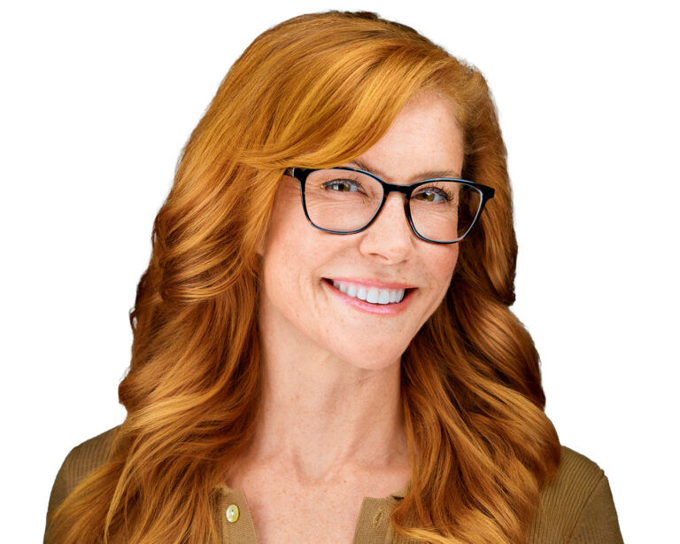 Professional headshot of a smiling woman with red hair and glasses, wearing a tan top, captured against a pure white background.