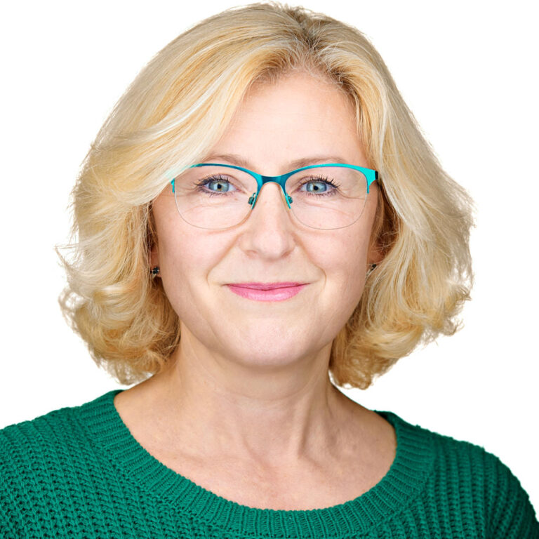 Professional headshot of a woman in green sweater with teal glasses, light background.