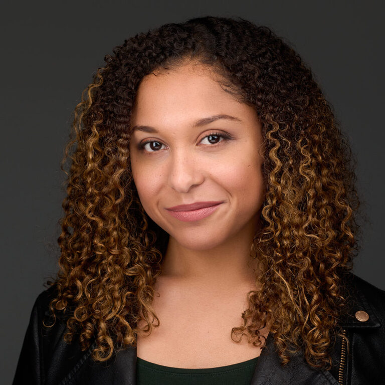Corporate portrait of a woman with curly hair, dark gray background.
