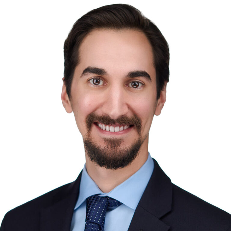 Studio headshot of a man in navy suit and tie, bright background.