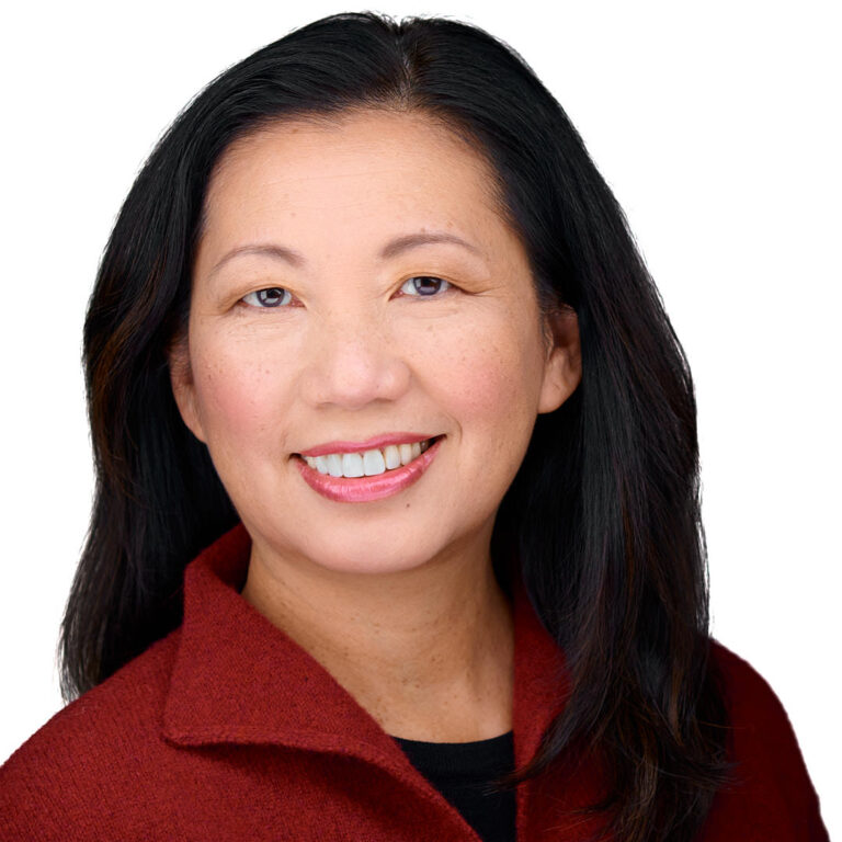 Executive headshot of a woman in red jacket, gray background.