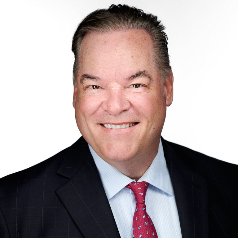 Executive portrait of a man in dark suit and red tie, light backdrop.
