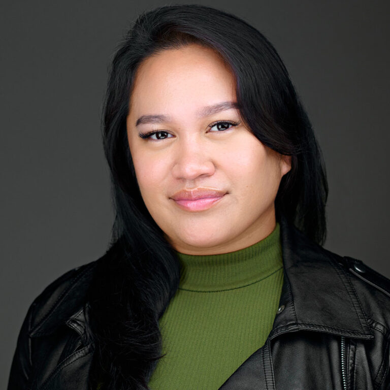 Professional portrait of a woman in green turtleneck and black jacket, dark background.
