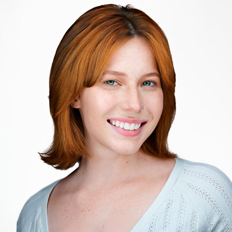 Studio headshot of a woman with auburn hair and light blouse, white background.