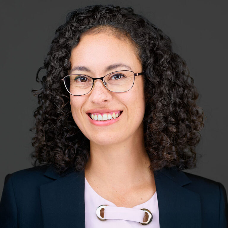 Professional portrait of a woman with curly hair, navy blazer, and white blouse.