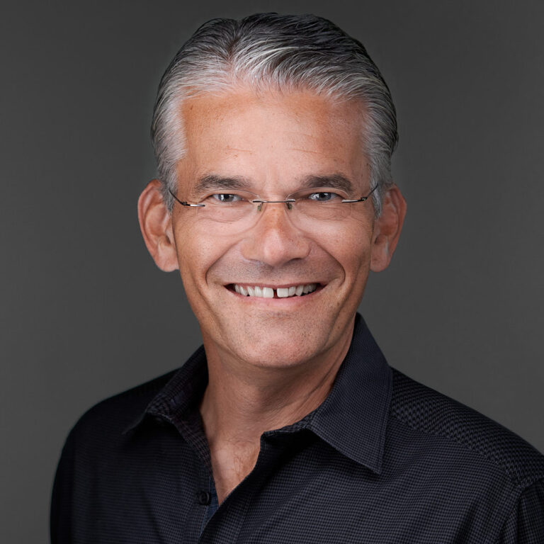 Professional headshot of a smiling man in a dark shirt and glasses, photographed by Dean Birinyi in Santa Clara.