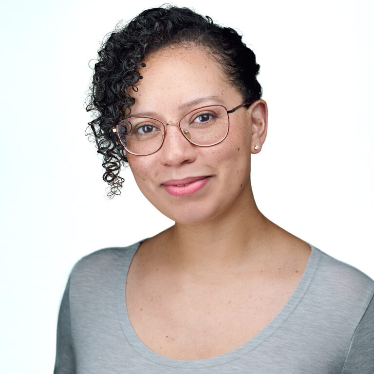 Professional headshot of a woman with short curly hair, glasses, and gray top, photographed by Dean Birinyi in Santa Clara.