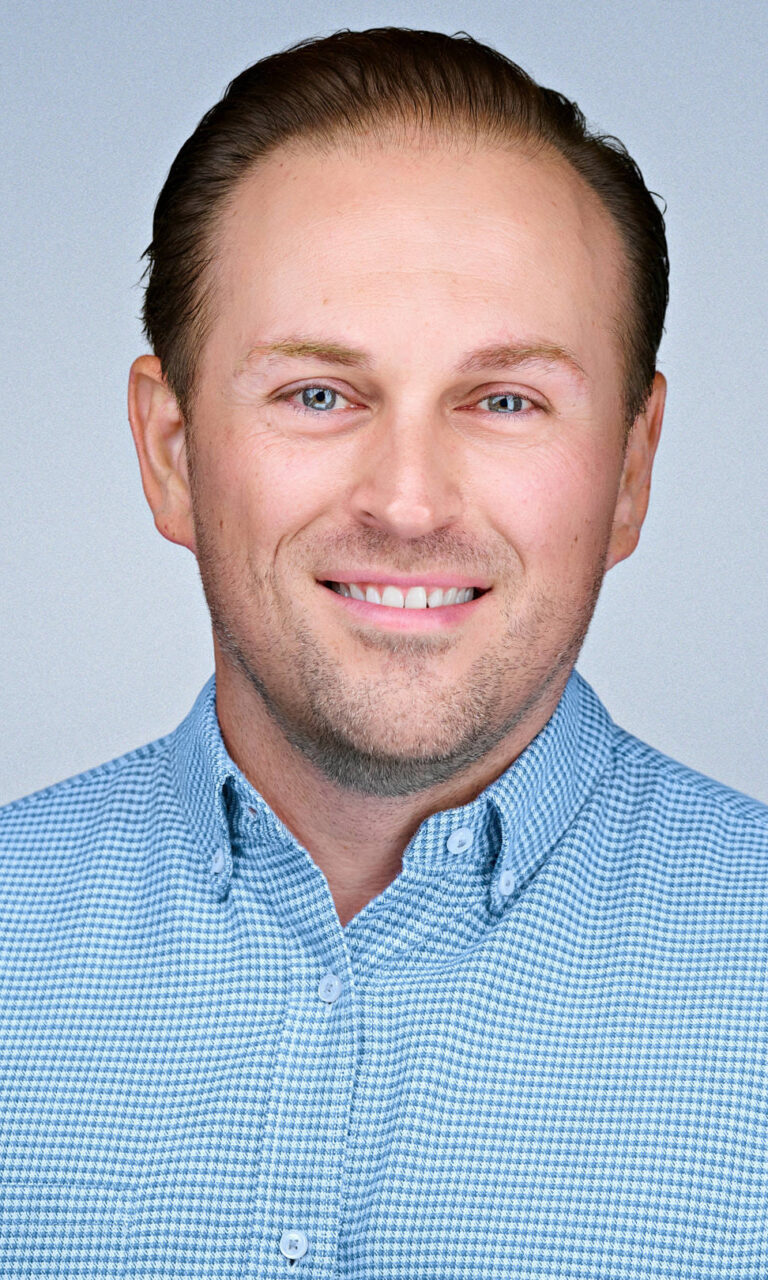 Professional corporate headshot of a smiling male professional wearing a light blue check button-down shirt, photographed by Dean Birinyi Photography in Santa Clara, California. Used on the company headshot system page to demonstrate brand-consistent portraits for Silicon Valley teams.