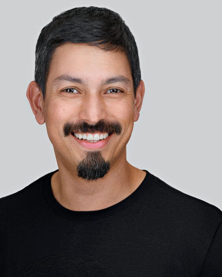 Professional corporate headshot of a smiling executive on a neutral gray background, showing polished lighting and expression consistent with brand-aligned company portraits.