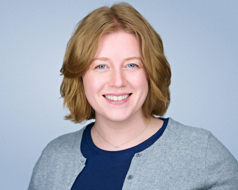 Professional headshot of a woman with short light-brown hair smiling against a light gray background.