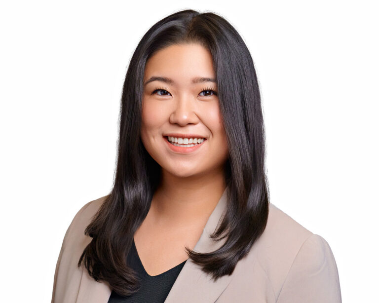 Professional studio headshot of a woman in a beige blazer, photographed against a white background with soft, even lighting.