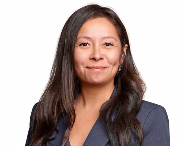 Professional headshot of a woman in a navy blazer, photographed with clean studio lighting on a white background.