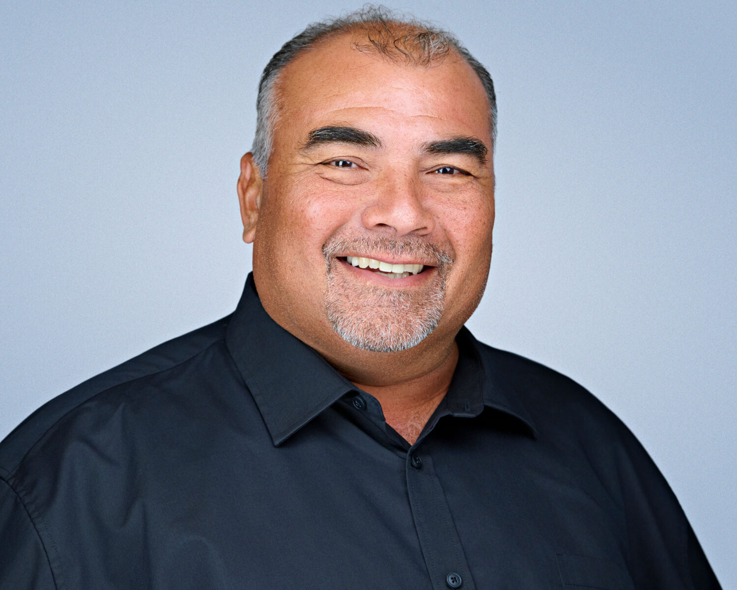 Professional headshot of a smiling man photographed in Santa Clara with soft studio lighting and a clean light-gray background.