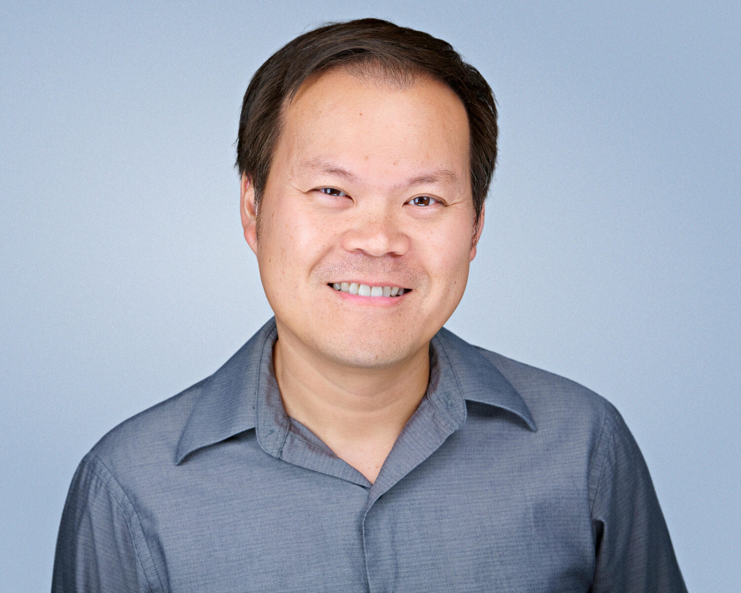 Professional headshot of a smiling man photographed in Santa Clara with soft studio lighting and a clean light-gray background.