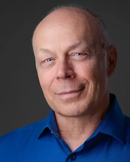 Dean Birinyi, professional photographer, in Santa Clara wearing a blue shirt with a dark minimalist background, photographed by Nina Pomeroy in Pleasanton, CA