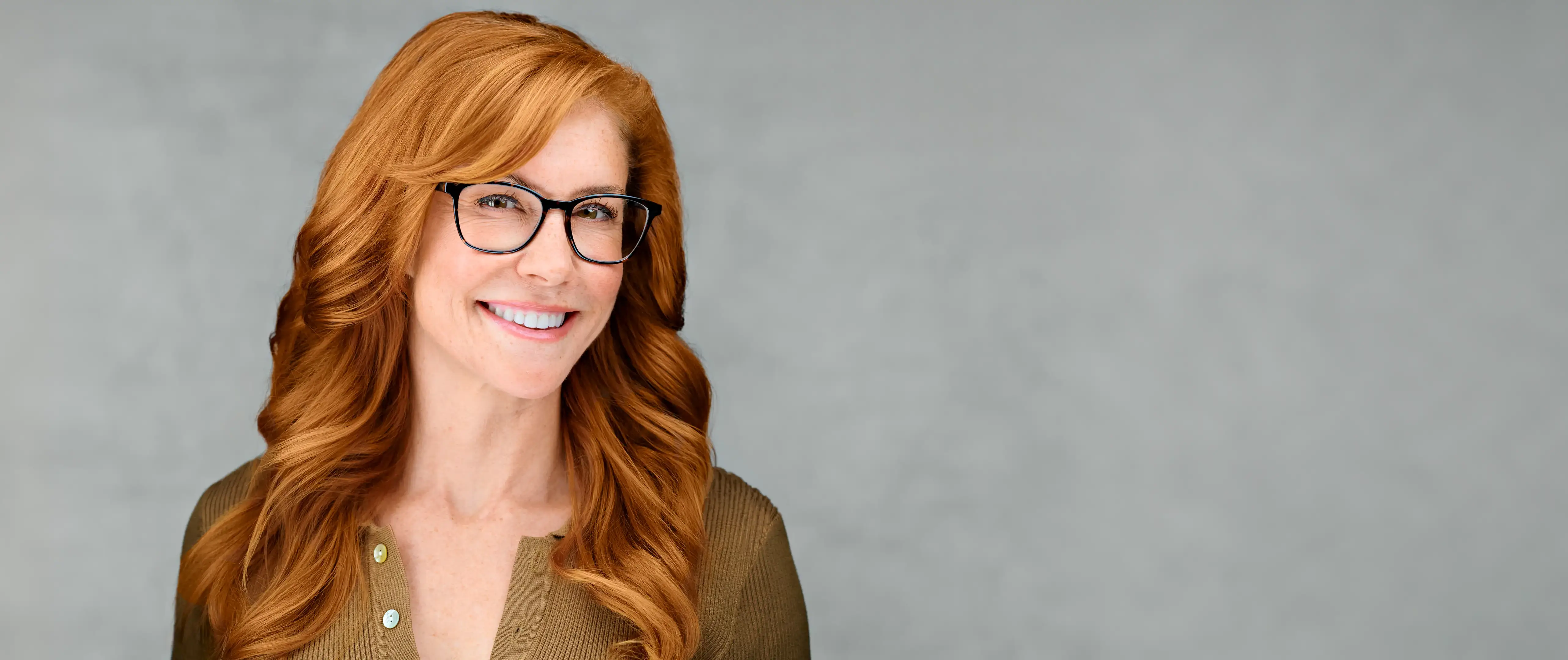 Professional company headshot of a smiling woman with red hair and glasses, photographed for polished team presentation.