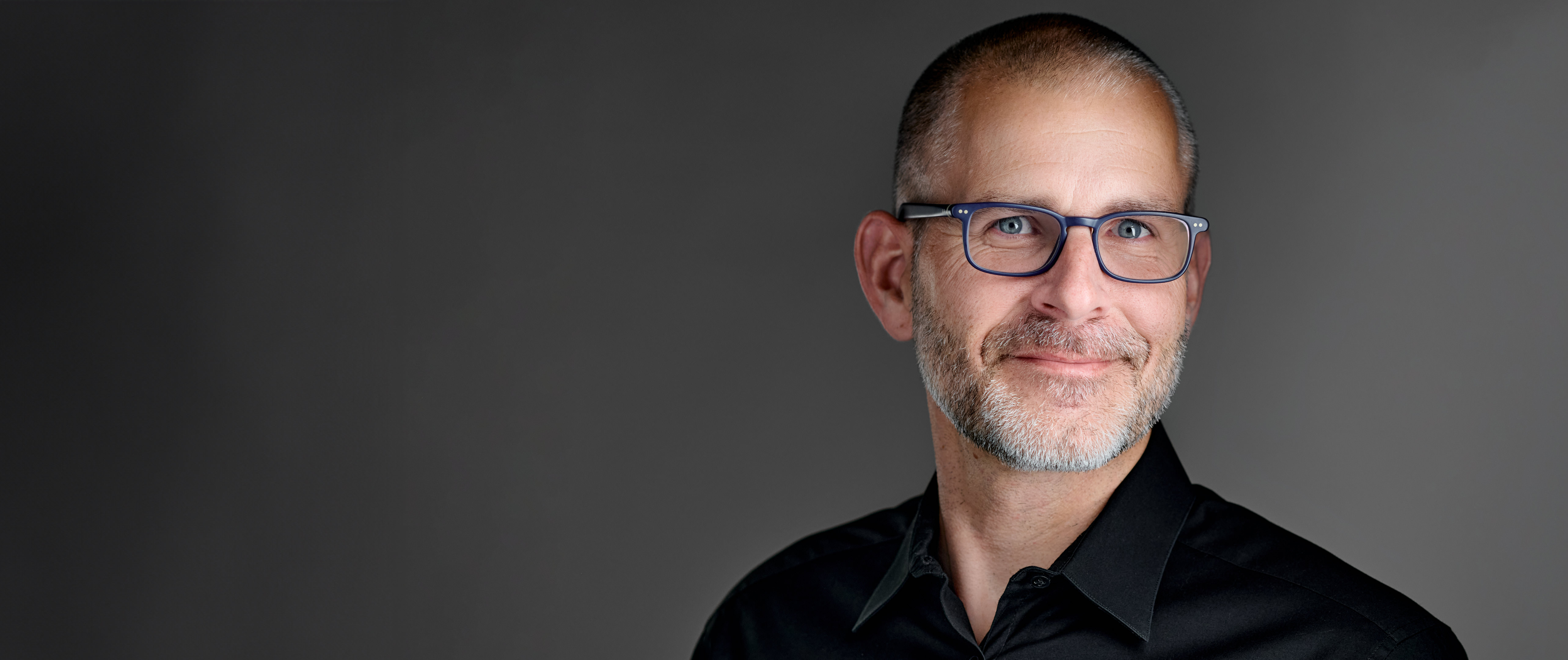 Professional headshot of Chris Edgette wearing glasses against a gray background.
