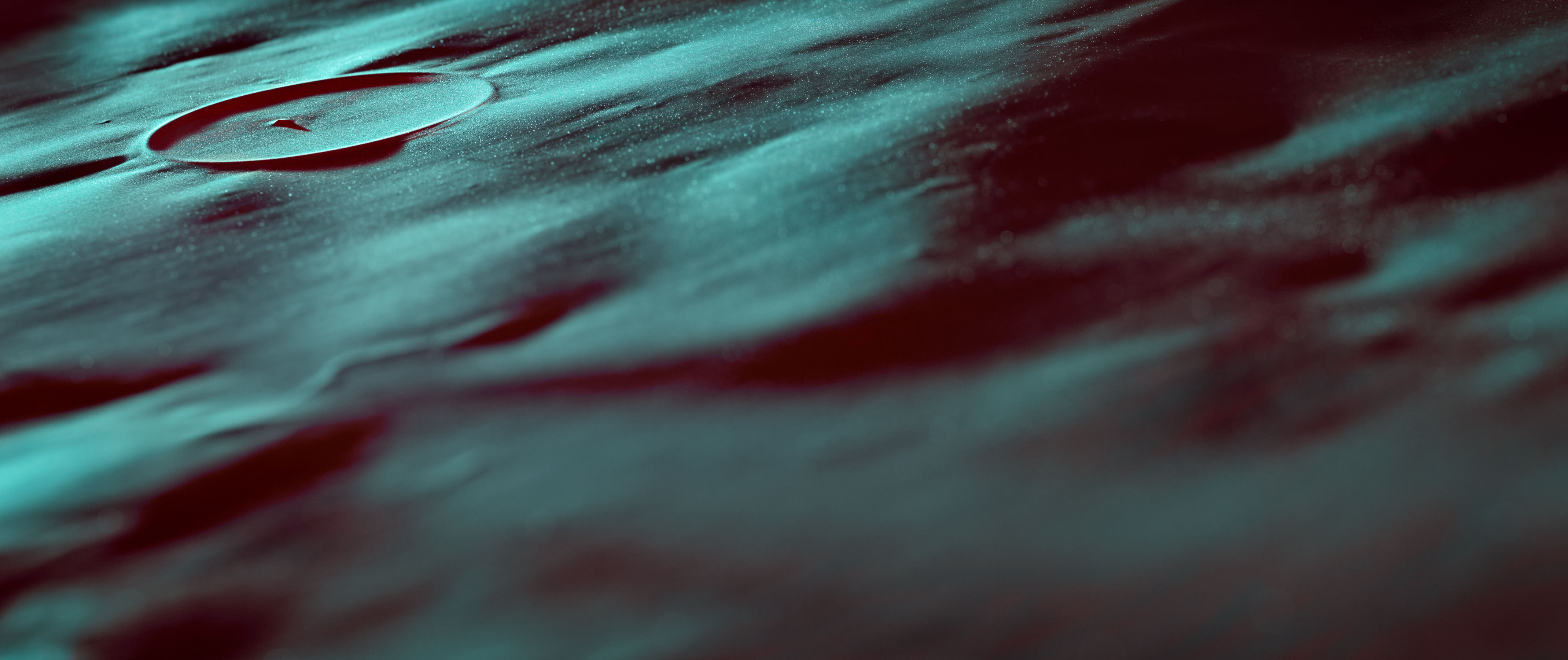 Abstract macro photograph from Isolation, showing teal light across a dark metal surface with shallow focus and a circular ridge.