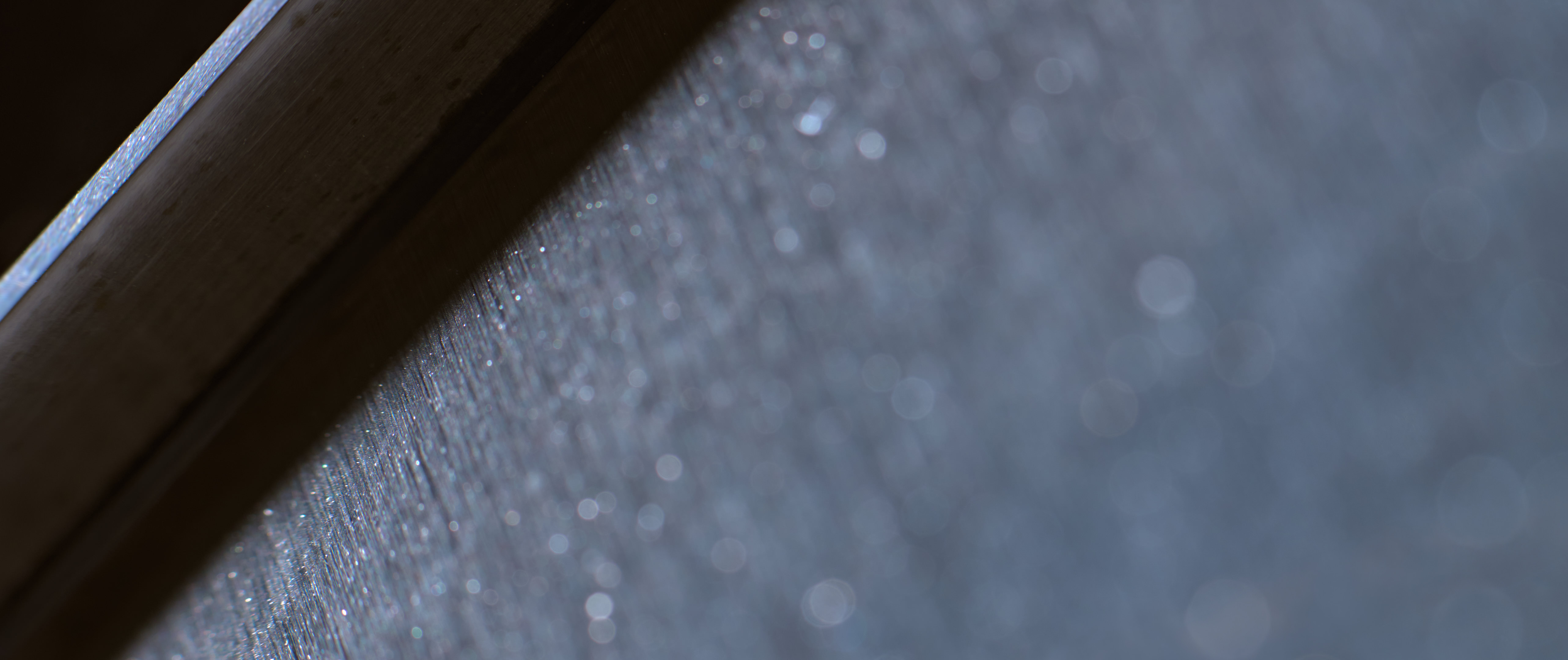 Abstract macro photograph of a dark diagonal edge dividing a shadowed surface from a softly shimmering blue-gray field.