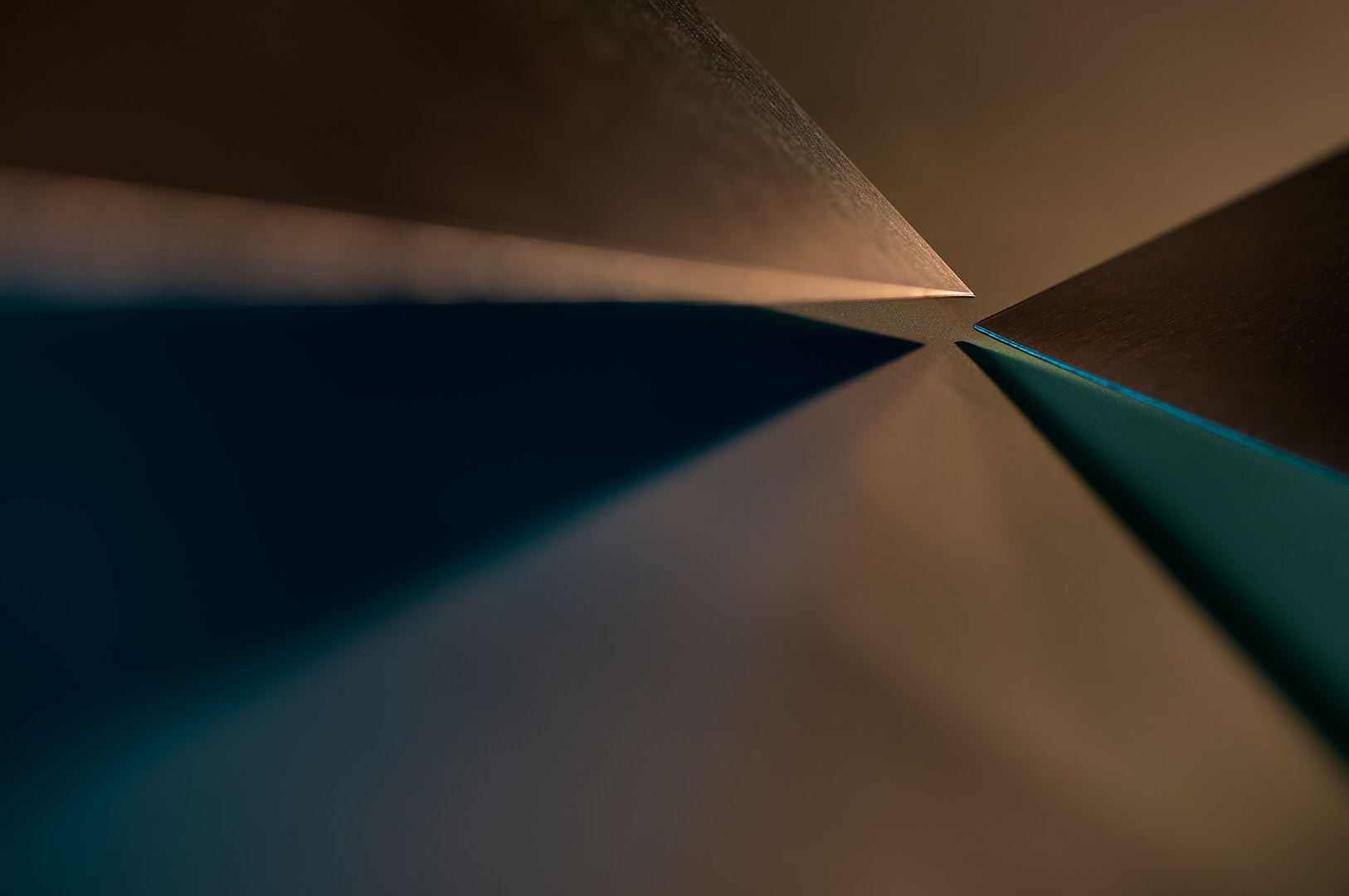 Abstract macro photograph of several pointed translucent forms converging toward a narrow central space, with layered color, reflected light, and opposing diagonal movement creating visual tension.