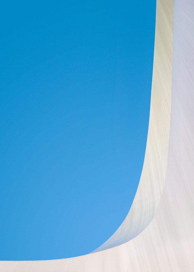 Abstract architectural detail of the Sundial Bridge showing a sweeping white curved surface with fine striations against a clear blue sky.