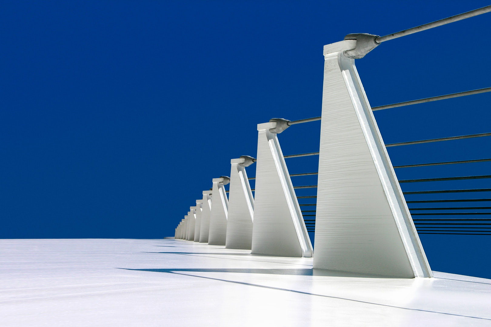 Low-angle view along the Sundial Bridge showing a receding row of white cable mounts and horizontal cables against a deep blue sky.