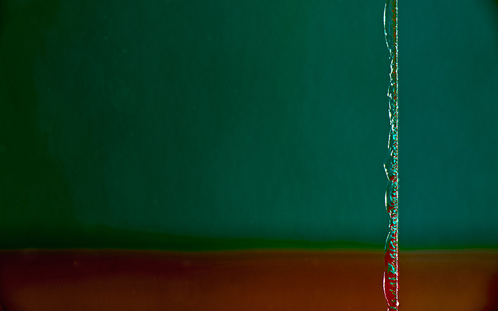 Minimal abstract photograph dominated by a dark green field, with a narrow irregular reflective vertical strip near the right edge and a muted red-brown band along the bottom.