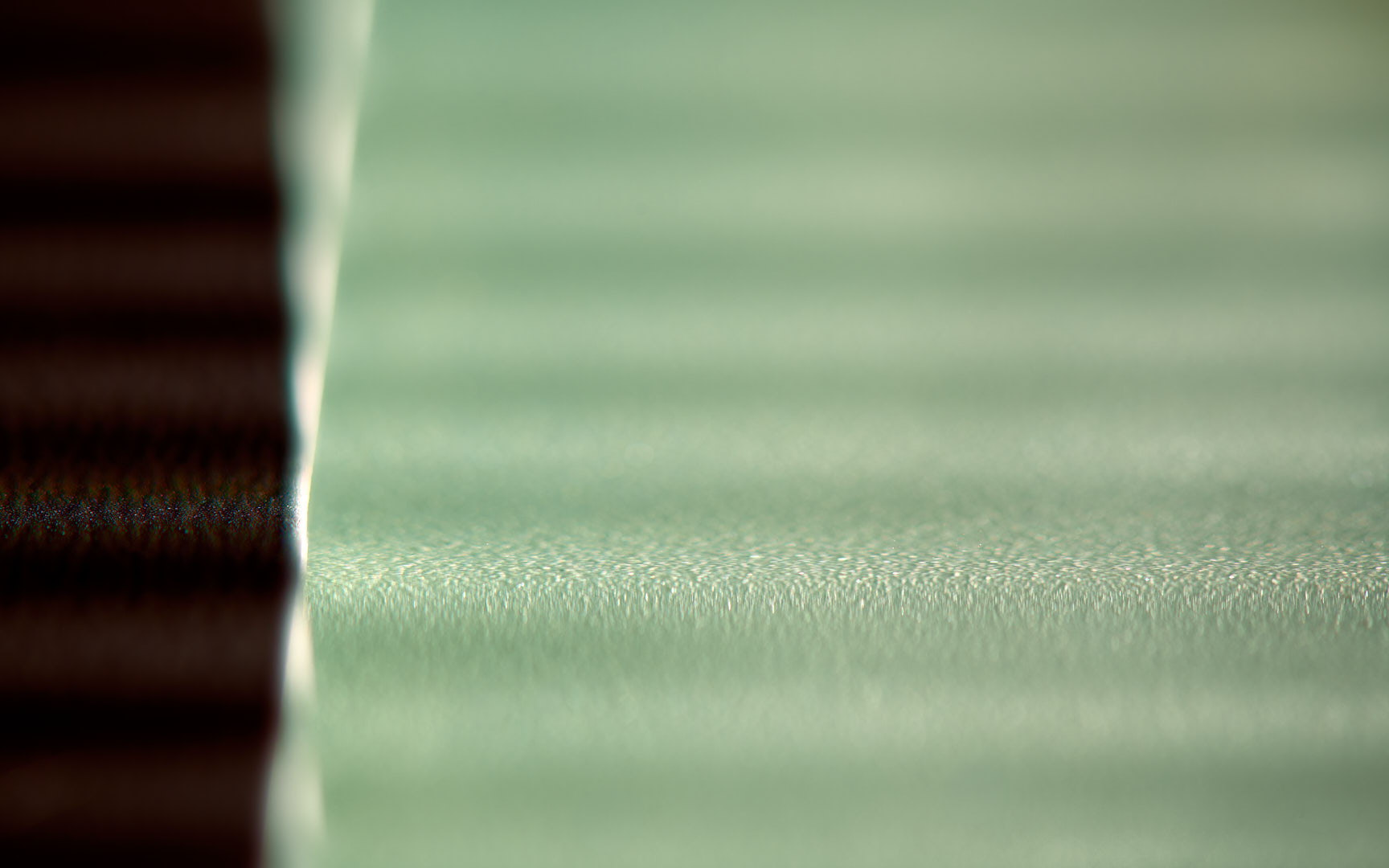 Abstract photograph of pale green horizontal planes meeting a dark vertical form at the left, separated by a narrow bright edge, with shallow repeating ridges extending across the frame.