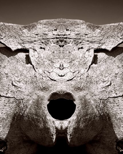 Symmetrical abstract composition of weathered stone with a dark circular opening at its center.