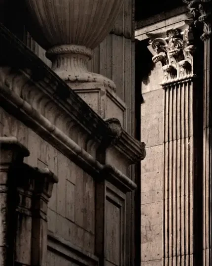 Warm monochrome detail of classical stone architecture with columns, carved capitals, and a diagonal balustrade.