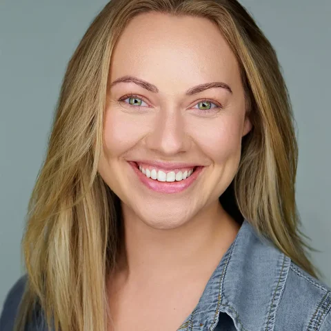 A smiling woman with blonde hair wearing a denim shirt against a soft gray background, photographed by Dean Birinyi in his Palo Alto commercial studio.