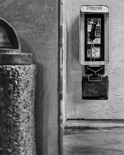 Black-and-white photograph of a payphone at dawn inside the Palo Alto California Avenue Caltrain Station.